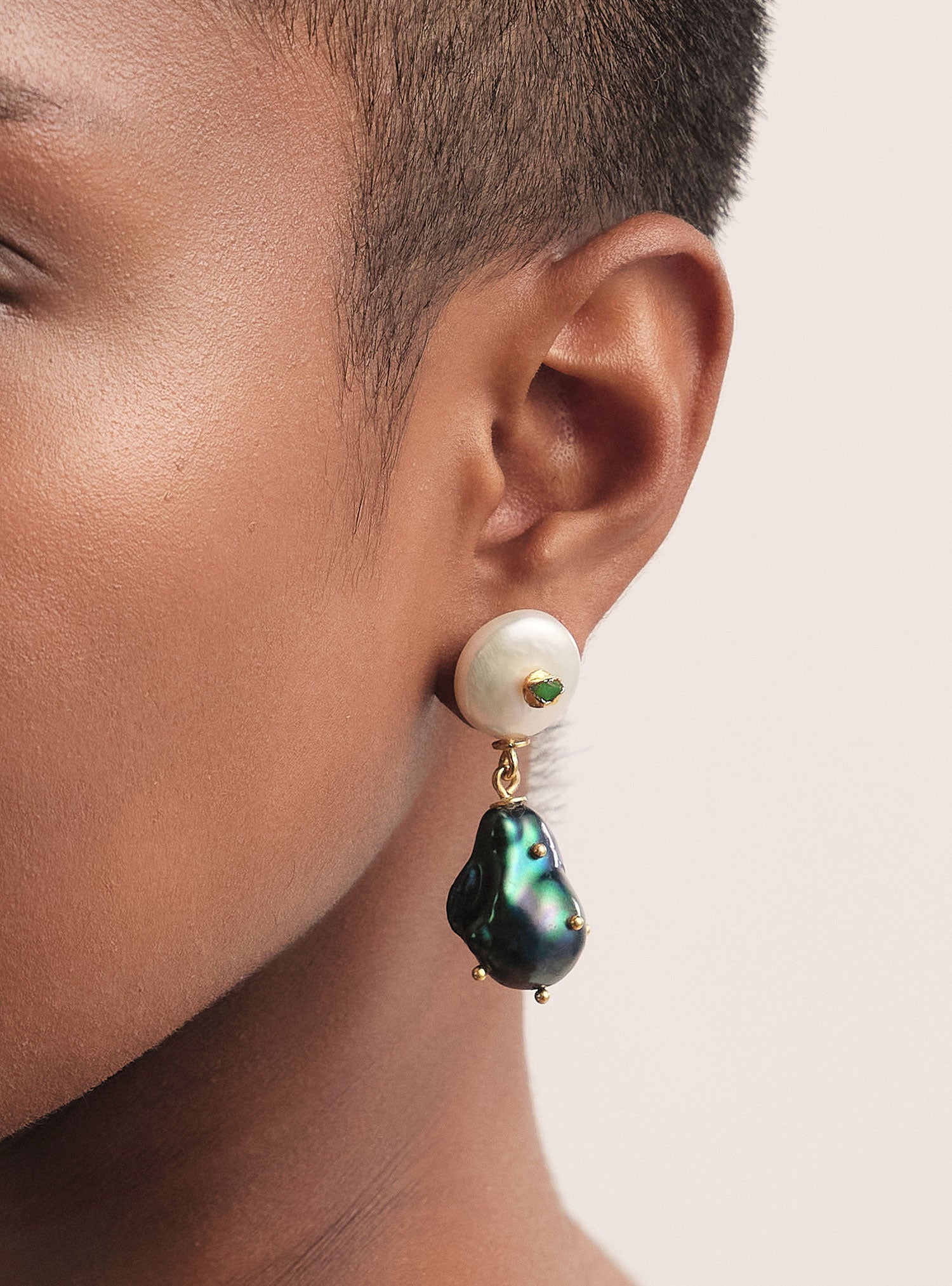 Aretes artesanales con perla blanca y perla barroca negra intervenida con esmeralda colombiana. Un diseño elegante y contemporáneo hecho a mano en Colombia.