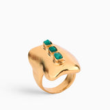 Anillo dorado con esmeraldas en bruto, diseñado con una estructura orgánica que fusiona modernidad y artesanía. Hecho a mano en bronce con baño de oro de 24K, una joya única y atemporal.