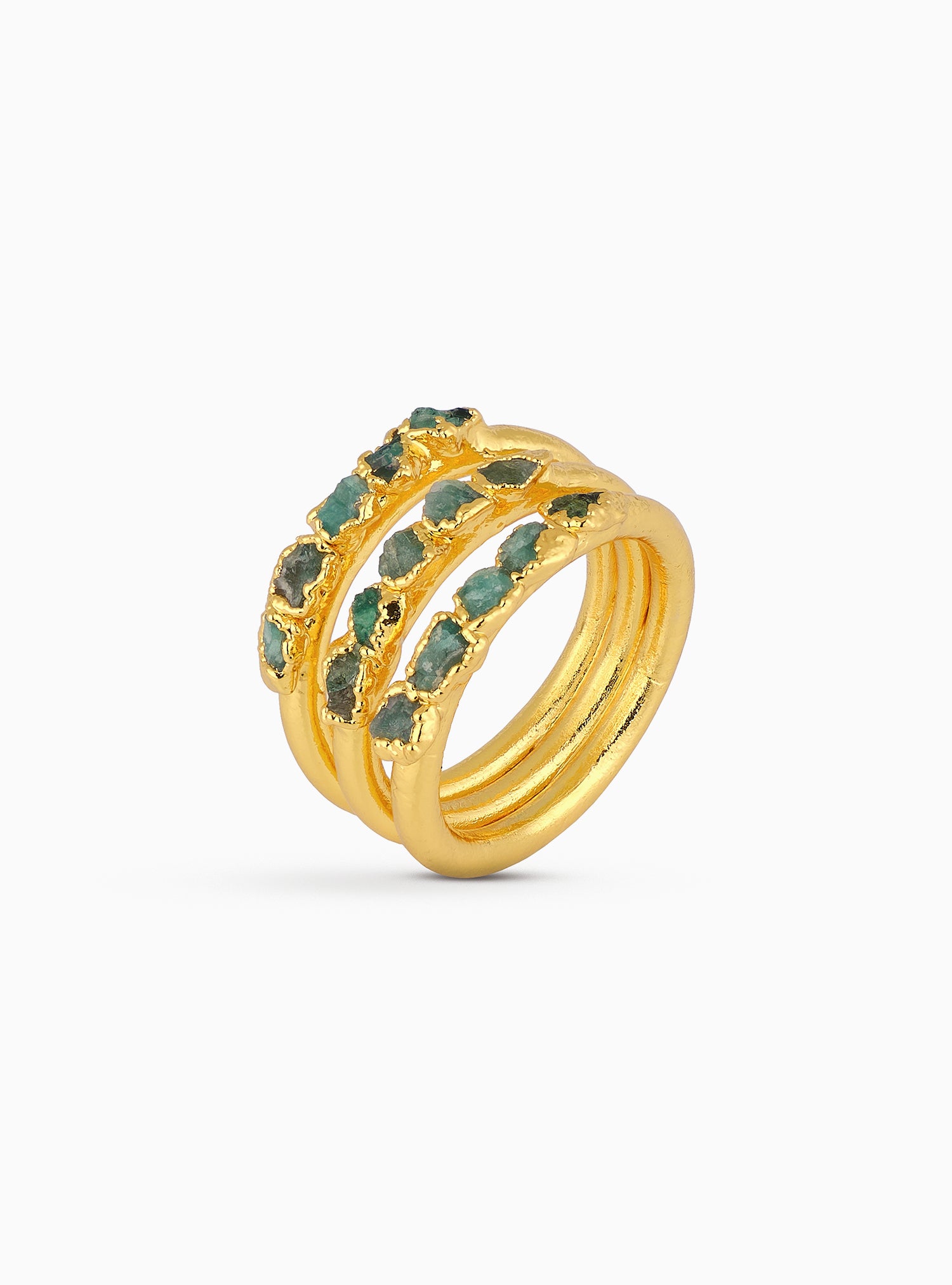Close-up editorial de un anillo elaborado en bronce con baño en oro, diseñado con esmeraldas colombianas en bruto cuidadosamente seleccionadas. Las piedras, con su textura natural y formas orgánicas, se integran en una estructura dorada que resalta la artesanía y el refinamiento de la pieza. La imagen muestra una joya de carácter, sofisticada y única, que combina trabajo manual minucioso con materiales excepcionales.