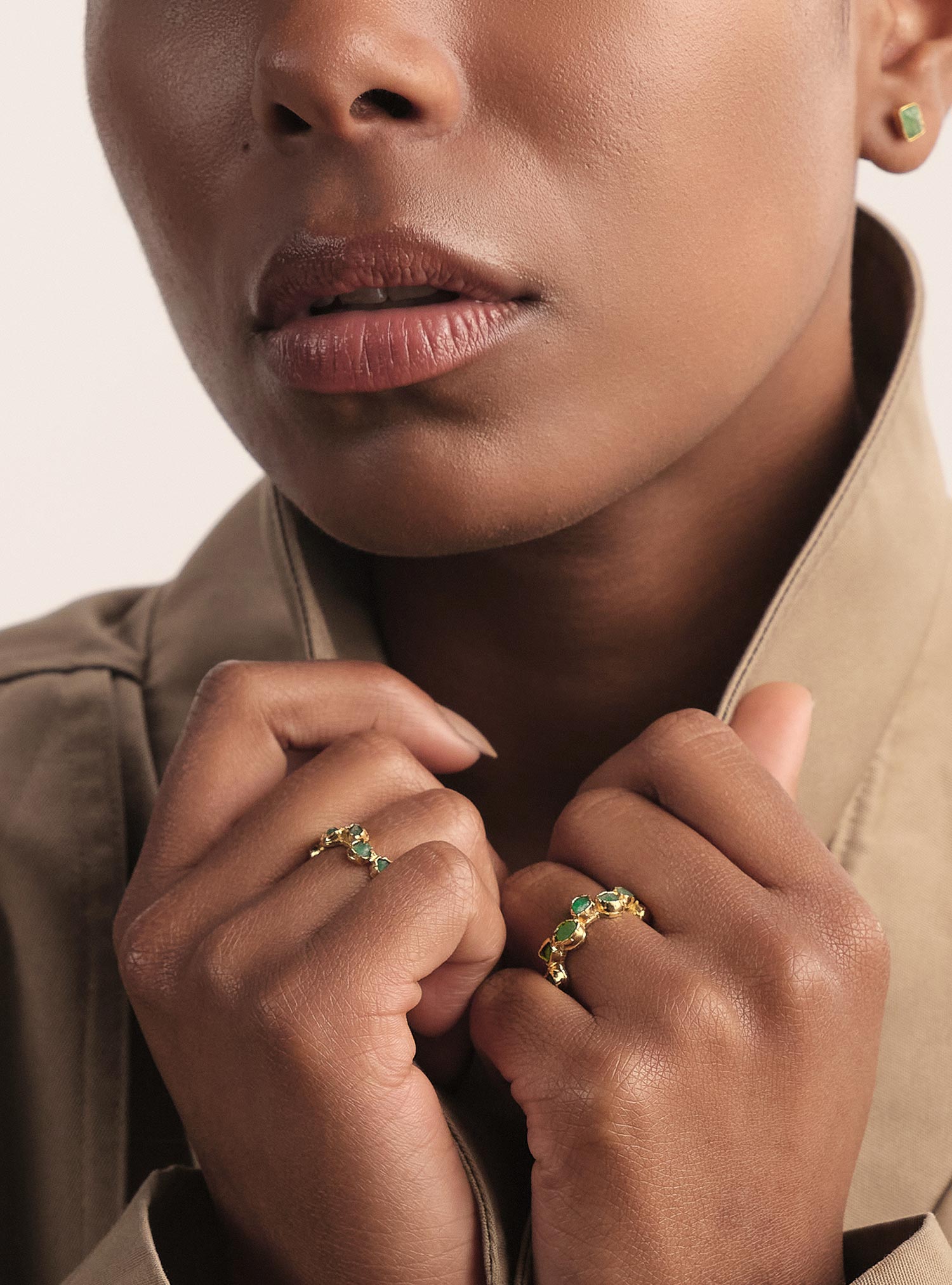 Close-up editorial de un anillo tipo infinito elaborado en bronce con baño en oro, diseñado con esmeraldas colombianas en bruto cuidadosamente montadas de forma artesanal. Su estructura continua y orgánica crea una silueta fluida que envuelve el dedo con elegancia. Las esmeraldas crudas aportan textura natural y un verde profundo, haciendo de este diseño una pieza distintiva, sofisticada y minuciosamente trabajada por Fenomena.