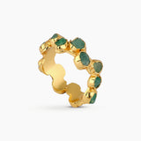 Imagen en primer plano de un anillo infinito compuesto por una cadena de esmeraldas crudas engastadas sobre bronce bañado en oro. Cada piedra conserva su forma orgánica, generando un diseño continuo que combina modernidad, delicadeza y artesanía elevada. La fotografía destaca la pureza del verde natural, el brillo del metal y la estética refinada que caracteriza a las piezas de Fenomena.