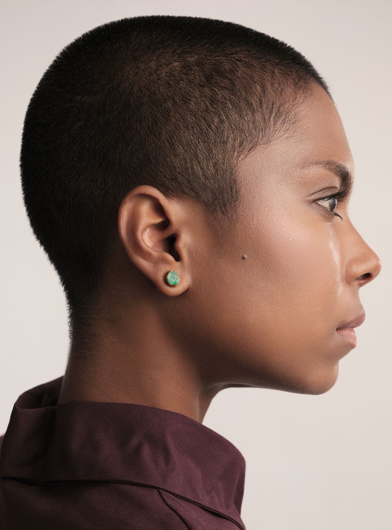 Retrato en perfil de un arete tipo stud elaborado con una esmeralda colombiana en bruto engastada de forma artesanal sobre una base de bronce con baño en oro. La piedra conserva su forma orgánica, mostrando la belleza natural y la textura cruda característica de las esmeraldas de Fenomena. La imagen resalta un diseño delicado, sofisticado y atemporal, ideal para quienes buscan piezas elevadas y naturalmente únicas.