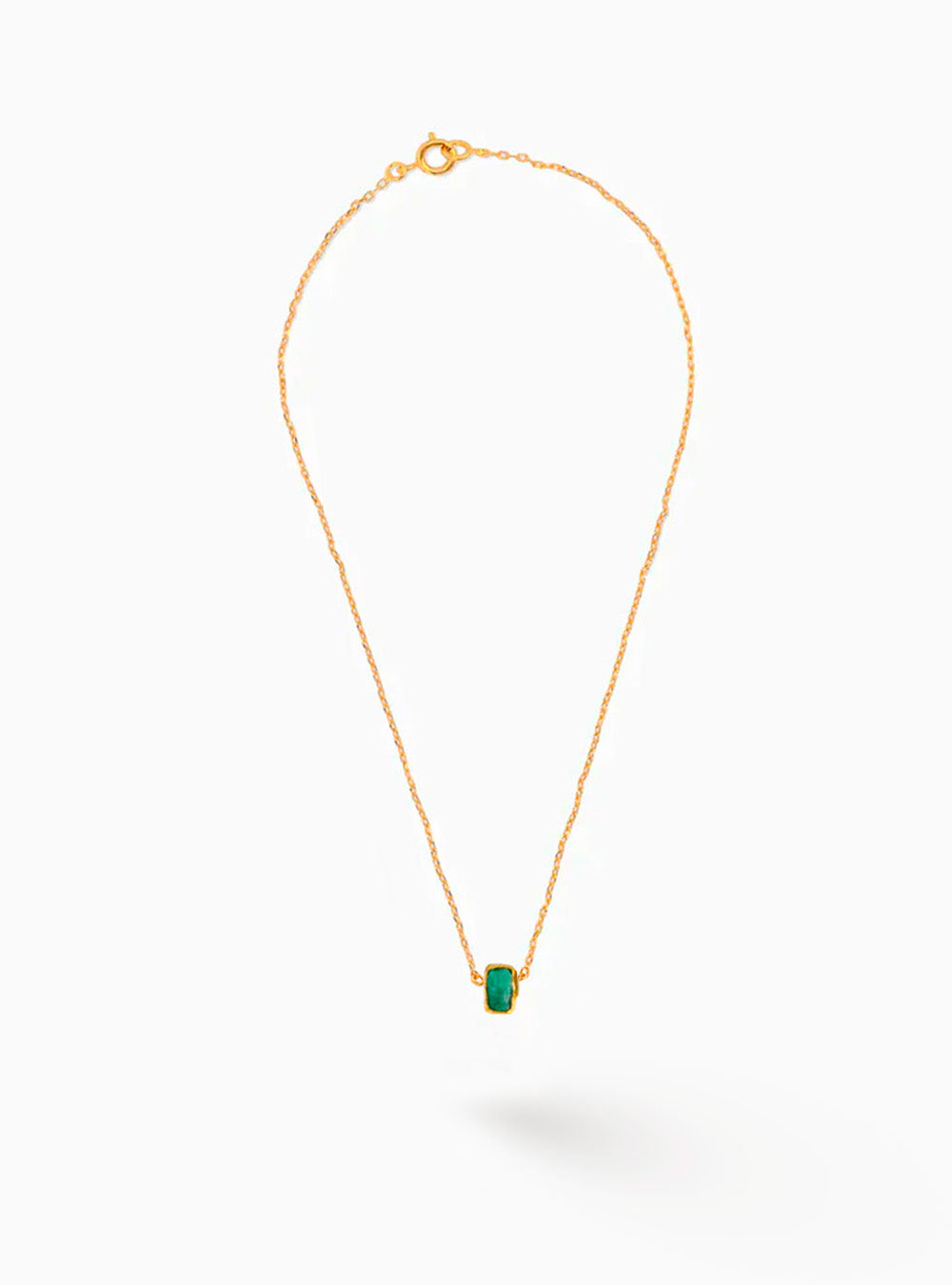 collar minimalista con cadena delgada en bronce con baño en oro, acompañado por un pequeño colgante de esmeralda cruda cuidadosamente seleccionada. Su silueta ligera y refinada realza la autenticidad de la piedra, creando una pieza discretamente sofisticada y versátil. La fotografía transmite la elegancia natural y el carácter artesanal característico de Fenomena.