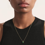 Close-up editorial de un collar básico compuesto por una cadena delicada en bronce con baño en oro y un dije de esmeralda colombiana en bruto. La piedra, en su estado natural, aporta un acento verde puro que contrasta de manera sutil con el dorado cálido del metal. La imagen destaca un diseño limpio, moderno y esencial, perfecto para el uso diario y representativo de la estética fina y artesanal de Fenomena.