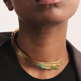 Close-up editorial de un collar de alta joyería compuesto por múltiples hilos de bronce bañados en oro, cuidadosamente ensamblados y terminados a mano. Dos esmeraldas colombianas en bruto, seleccionadas por su forma orgánica y su rareza, se integran de manera sutil y precisa en la pieza, aportando un acento verde puro que eleva el diseño. La imagen destaca el refinamiento del acabado, la delicadeza del volumen y la esencia minimalista de un collar exquisitamente trabajado por Fenomena.