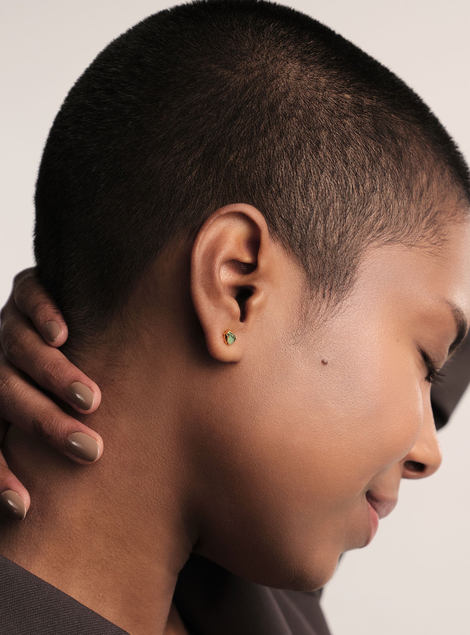 Primer plano editorial de unos aretes pequeños en bronce con baño en oro, diseñados para el día a día. Cada pieza incorpora una esmeralda colombiana en bruto, seleccionada por su forma orgánica y su carácter natural, aportando un contraste exquisito entre el dorado intenso y el verde profundo de la piedra cruda. Una joya altamente elaborada, de presencia artística y acabado impecable, distintiva de la estética refinada de Fenomena.