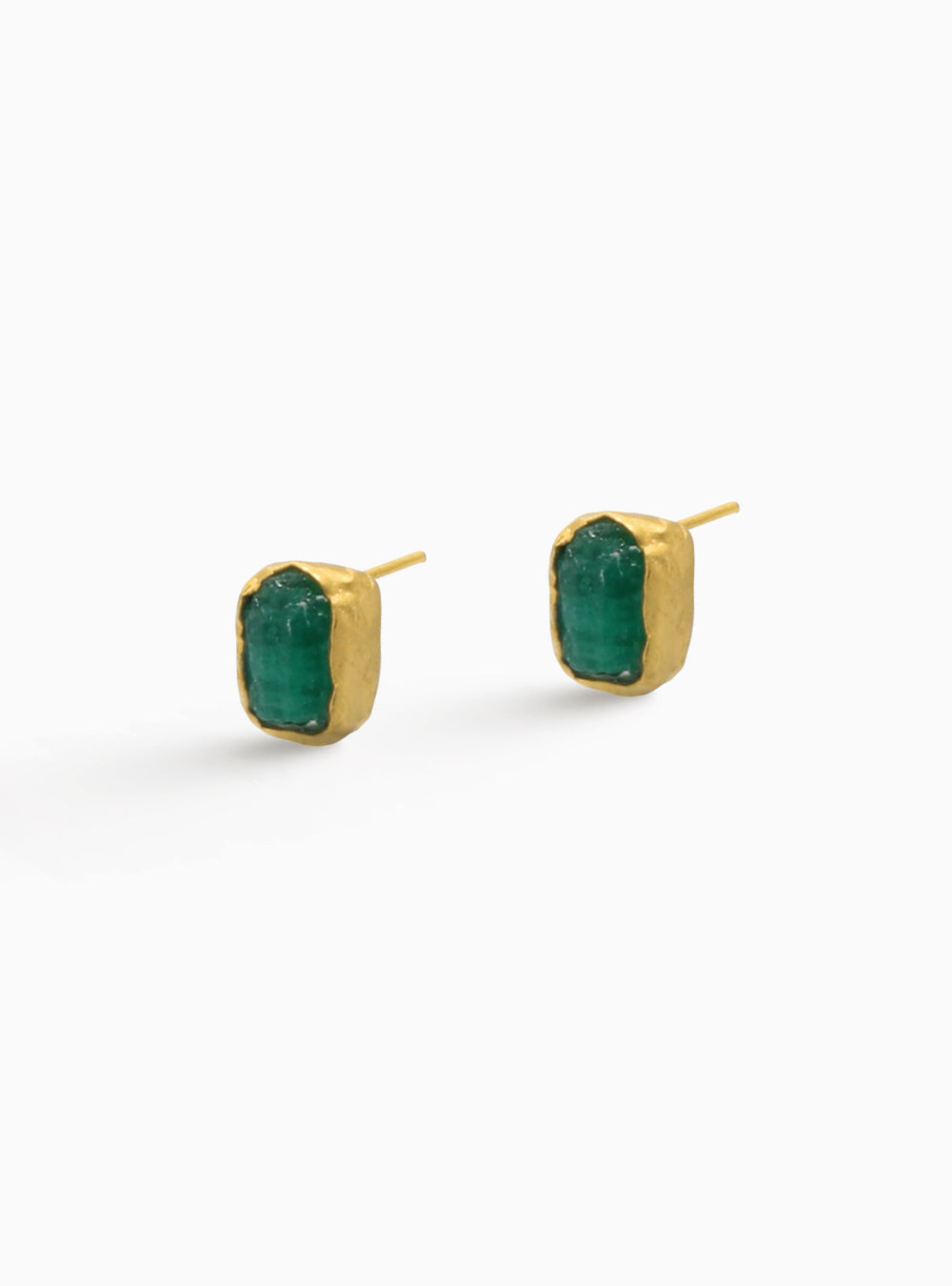Aretes tipo stud en bronce con baño en oro y esmeralda colombiana en bruto. Diseño minimalista con piedra natural sin pulir, que resalta su forma orgánica y su color verde característico. Joya artesanal, perfecta para uso diario o combinaciones delicadas. Fotografía ideal para catálogo de ecommerce.