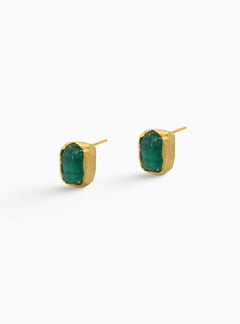 Aretes tipo stud en bronce con baño en oro y esmeralda colombiana en bruto. Diseño minimalista con piedra natural sin pulir, que resalta su forma orgánica y su color verde característico. Joya artesanal, perfecta para uso diario o combinaciones delicadas. Fotografía ideal para catálogo de ecommerce.